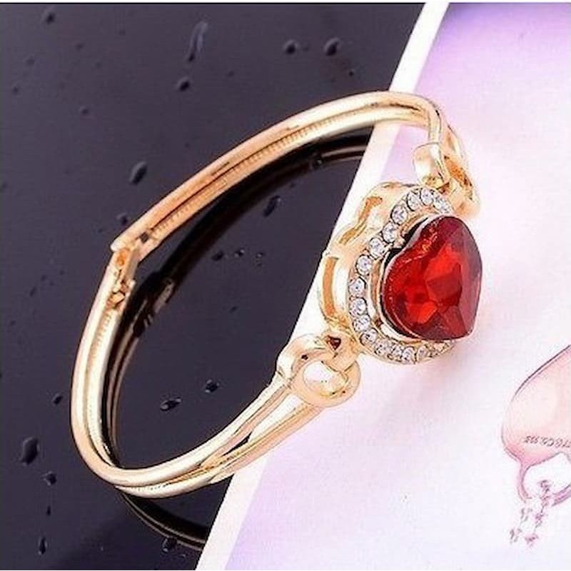 Brazalete rígido de acero inoxidable dorado con colgante de corazón en piedra granate y detalles de circonitas blancas.