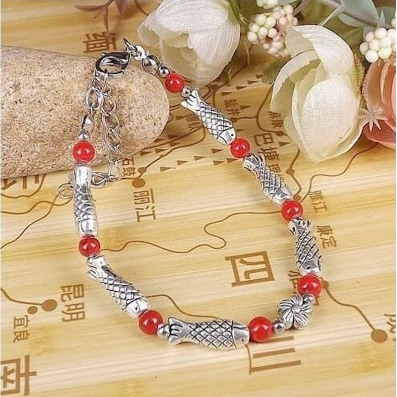 Pulsera de acero con acabado plata de estilo étnico tibetano decorada con figuras de peces y piedras rojas.