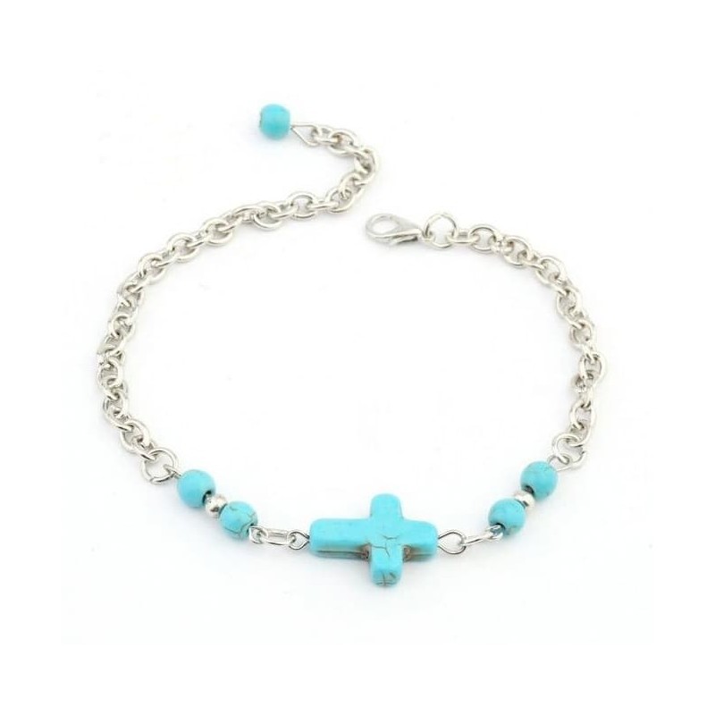 Cadena fina chapada en plata para muñeca o tobillo con un dije central en forma de cruz de color turquesa vibrante.