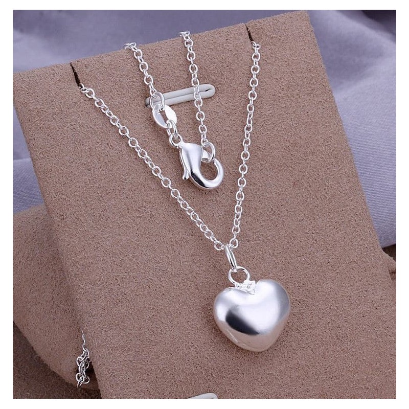 Cadena fina de acero plateado con un dije central pequeño en forma de corazón pulido y de superficie convexa que refleja la luz.