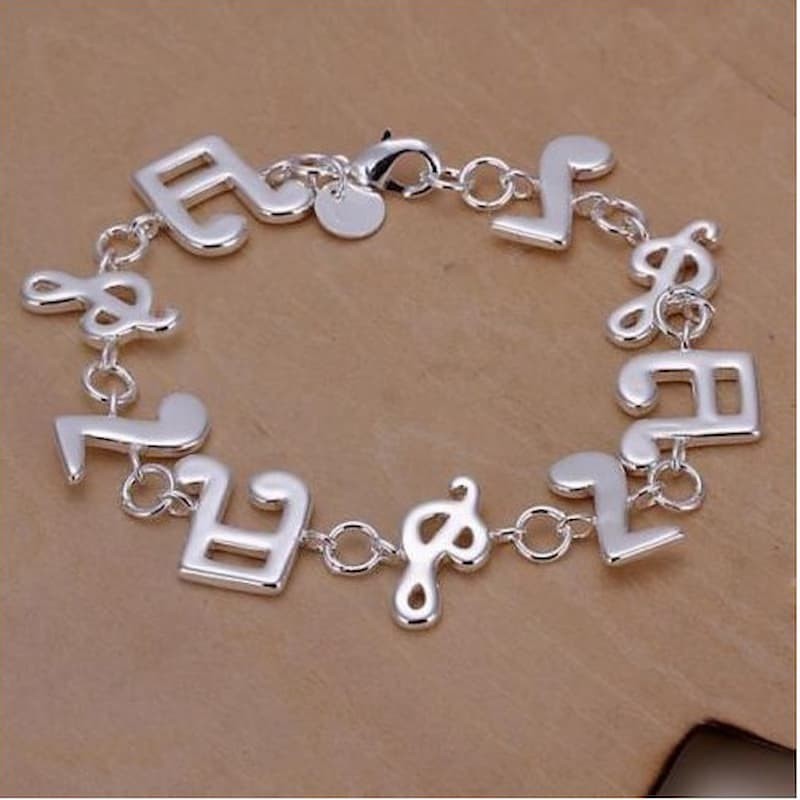 Brazalete rígido de acero con baño de plata de ley 925 y diseño calado de notas musicales con acabado pulido espejo.